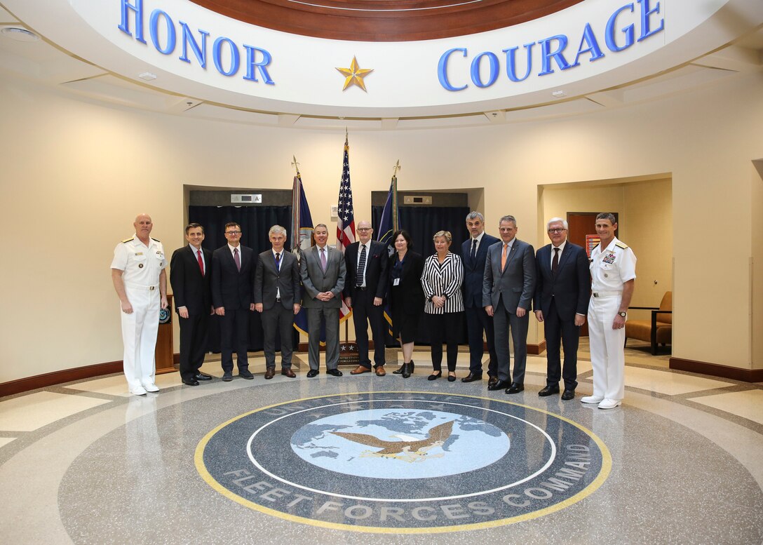 A group of service members and civilians stand for a photo in a building.