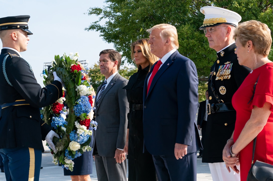 The president and first lady stand in front of a wreath, flanked by the defense secretary and his wife, and the Joint Chiefs chairman and his wife.