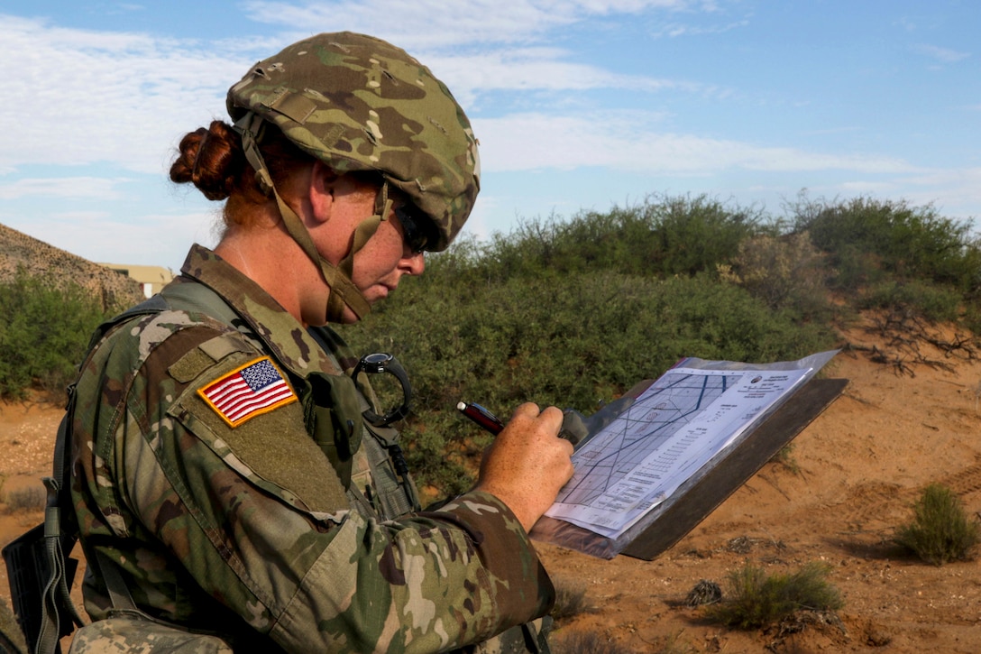 A soldier studies a map in a grassy area.
