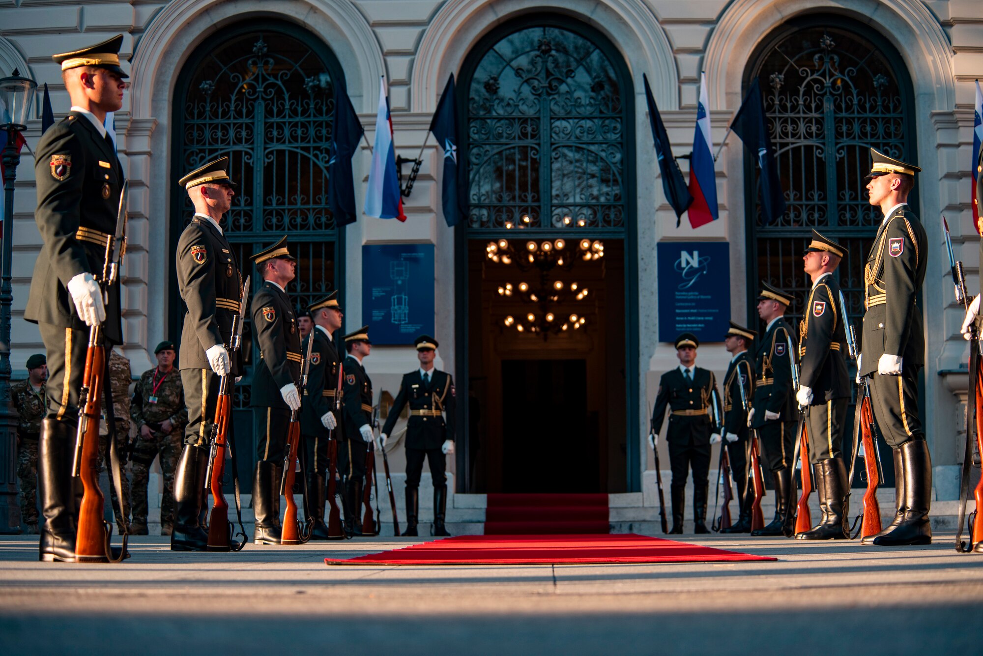 Troops flank a red carpet outside an ornate building entrance.