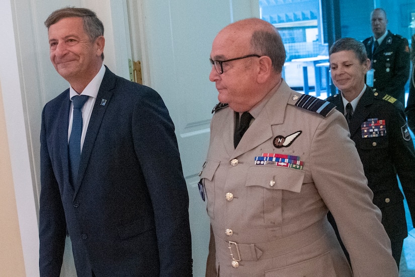 Military officers walk with a civilian.