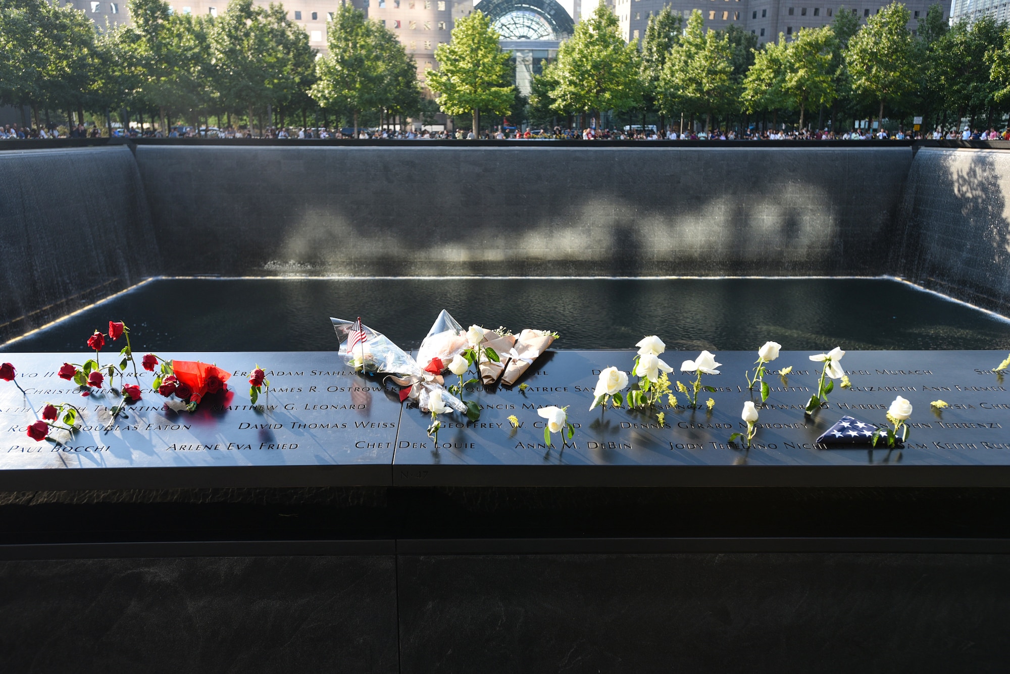 Family members placed flowers on the engraved names of the Sept. 11 memorial in New York City Sept. 11, 2019. People come from all over the world to pay their respects to the fallen individuals and their families from the attacks of Sept. 11, 2001. Two waterfalls were built in place of the twin towers as a memorial to the 2,977 people killed, with each name engraved in the stone. (U.S. Air Force photo by Airman 1st Class Ariel Owings)
