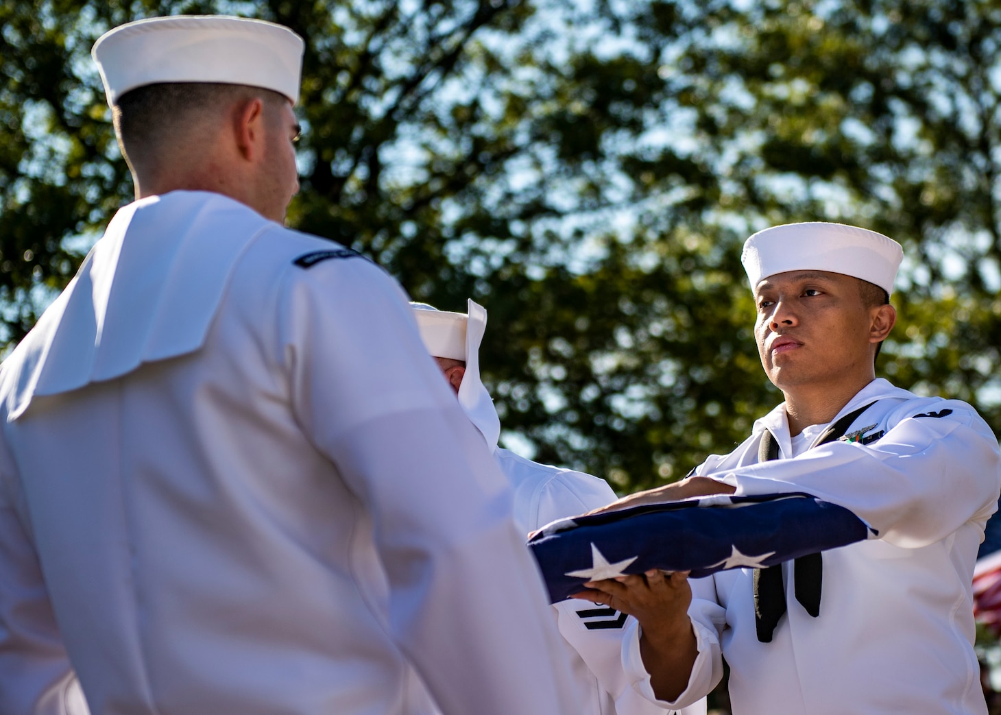 A sailor passes a folded flag to another sailor.