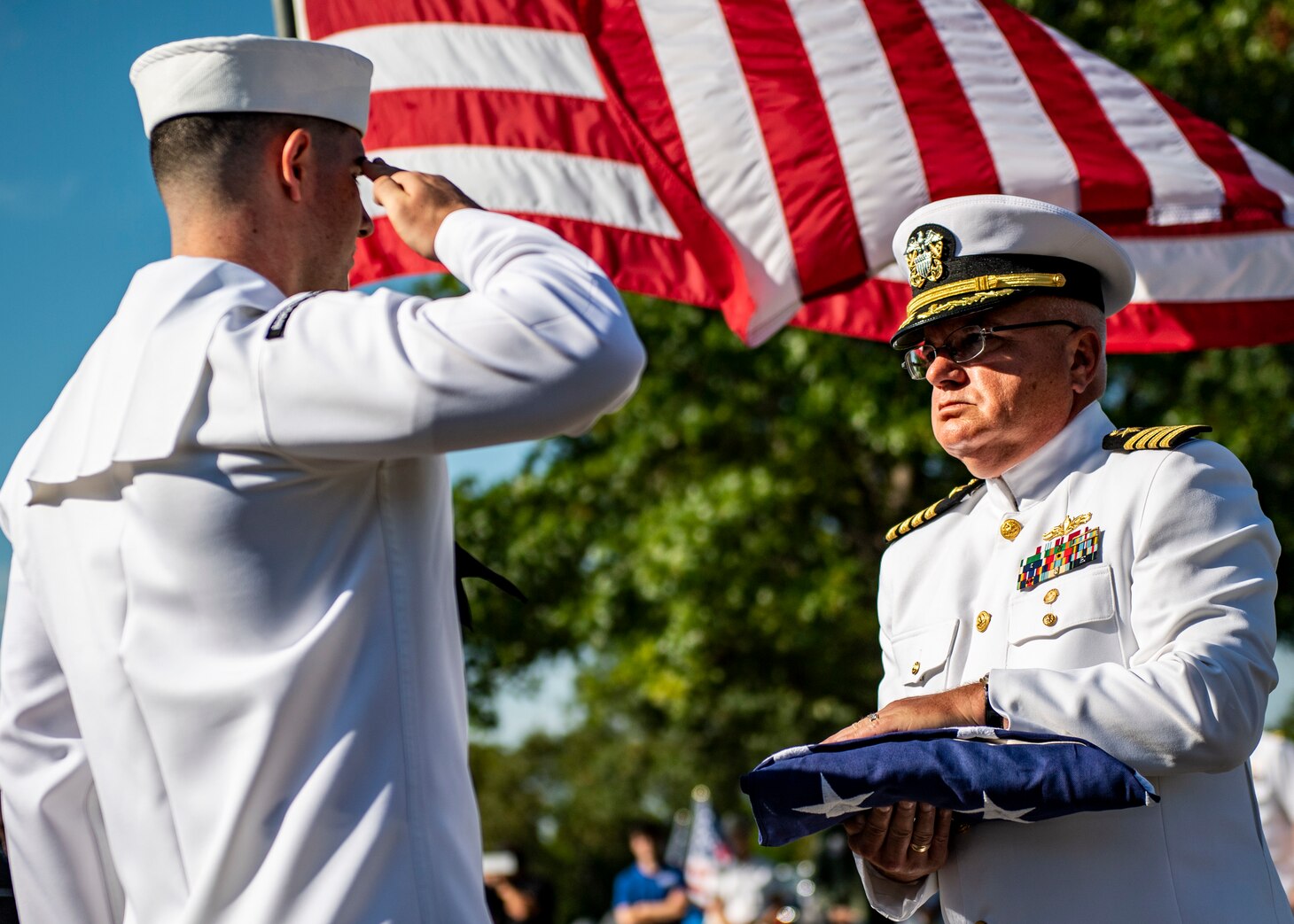 A sailor salutes another sailor with a flag.