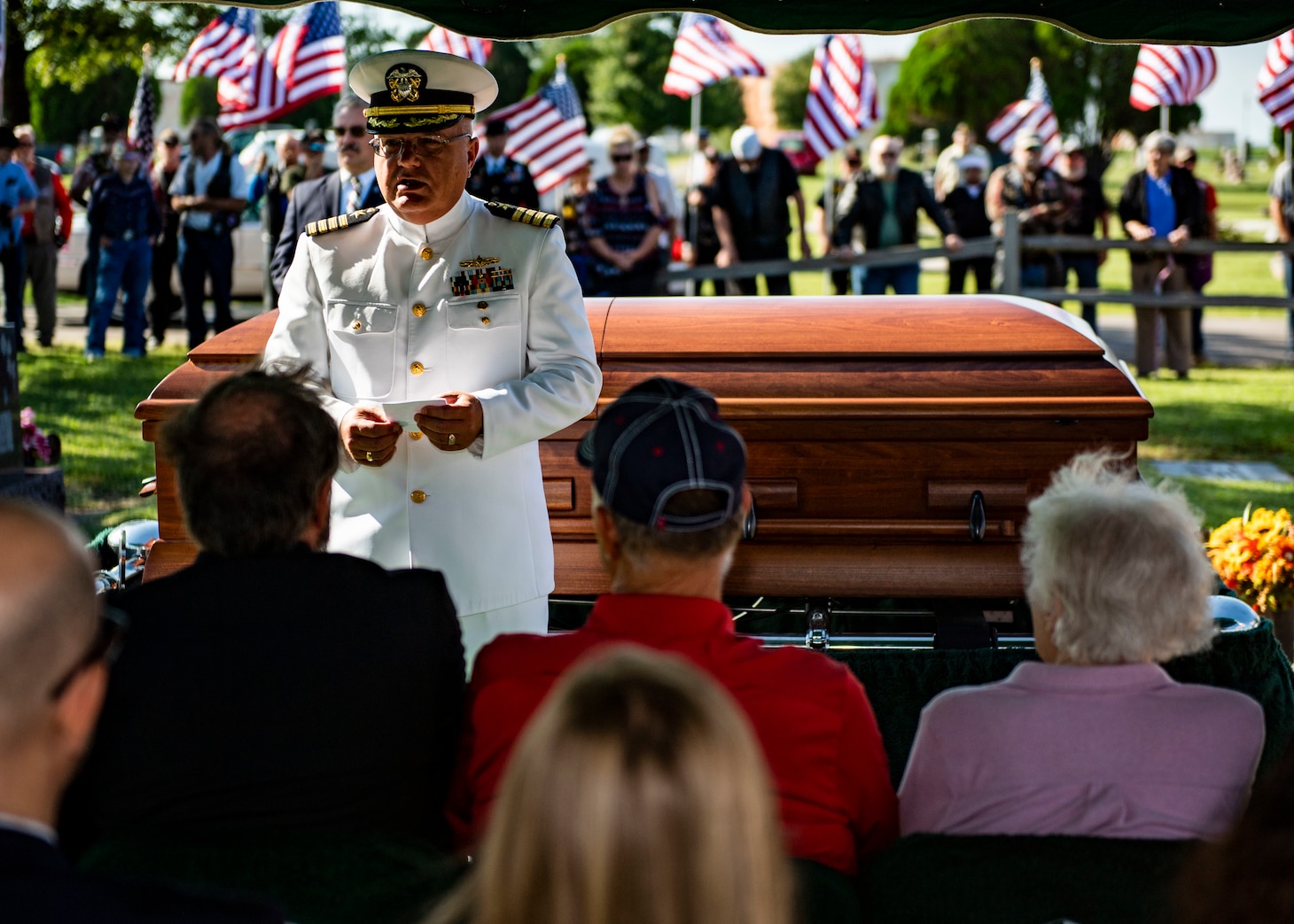 A sailor delivers remarks in front of a casket.