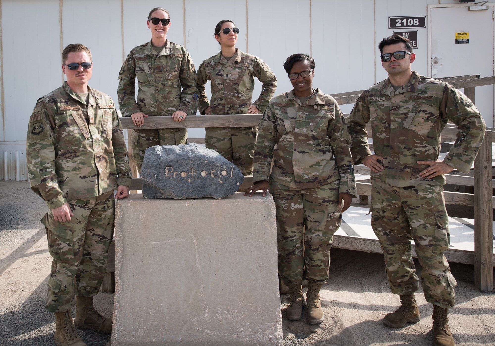 The 386th Air Expeditionary Wing protocol team poses for a photo outside their office at Ali al Salem Air Base, Kuwait, Aug. 15, 2019. Left to Right: Tech. Sgt. Tyler Shepherd, NCO-in-charge of protocol, deployed from Moody Air Force Base, Georgia; Capt. Rosa-Mae Bacon, chief of protocol, deployed from Davis-Monthan AFB, Arizona; 1st Lt. Kassandra Prusko, deputy chief of protocol, deployed from Andrews AFB, Maryland; Staff Sgt. Courtney Lansden, protocol specialist, deployed from Offutt AFB, Nebraska; and Tech. Sgt. Diego Casillas, superintendent of protocol; deployed from Los Angeles AFB, California. (U.S. Air Force photo by Tech. Sgt. Daniel Martinez)