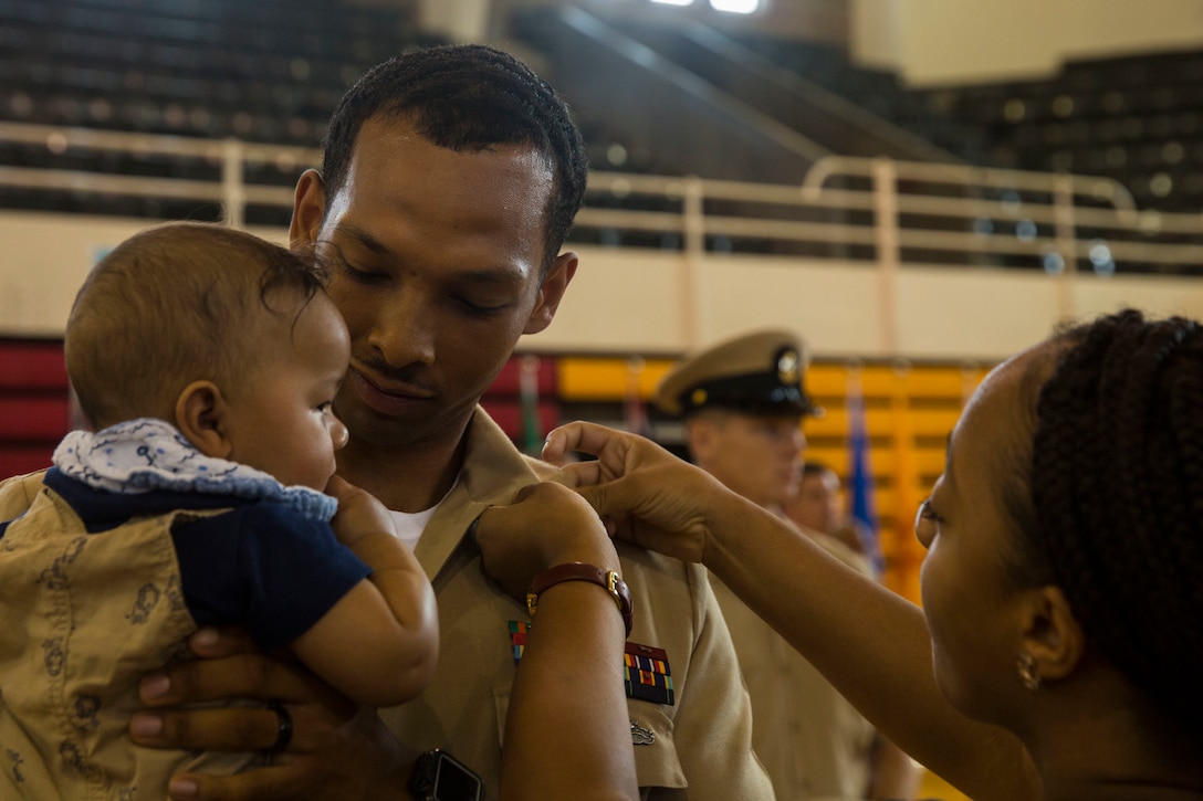 A U.S. Navy Sailor holds his child as he is pinned with chief anchors by his wife during the Chief Petty Officer Pinning Ceremony on Camp Lejeune, N.C., Sept. 13, 2019. Thirty-three chief selects were pinned to the rank of chief petty officer and among them were two Marines that earned the title of honorary chief petty officer. Before the chief selects can pin on their new rank, they must go through a six-week initiation course in order to instill the trust that is inherent with the donning of the uniform of a chief. (U.S. Marine Corps photo by Cpl. Leynard Plazo)