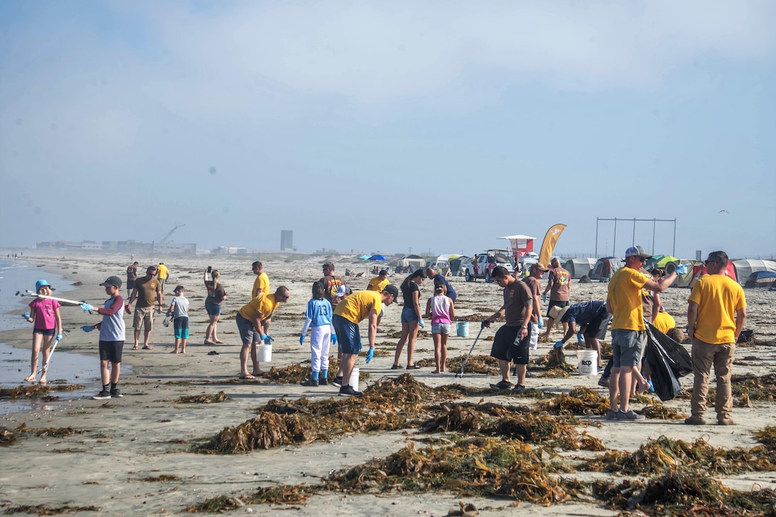 Sailors and military family members pick up debris on a beach.