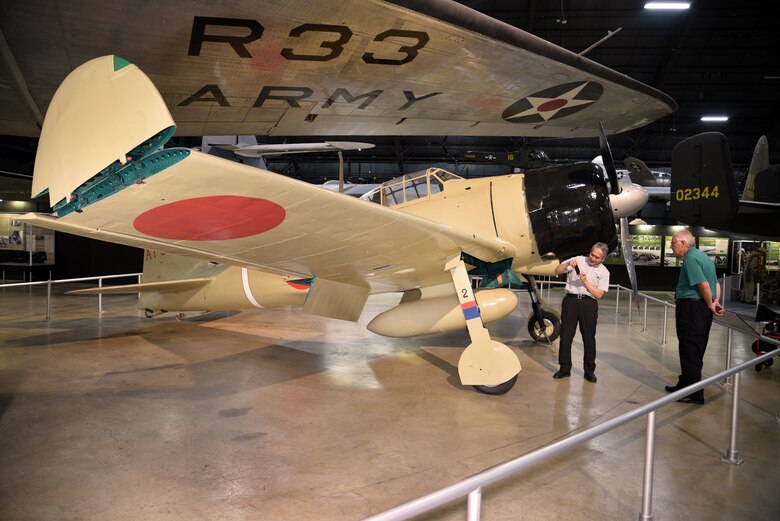 Photo of two people at Japanese Zero aircraft from World War II.