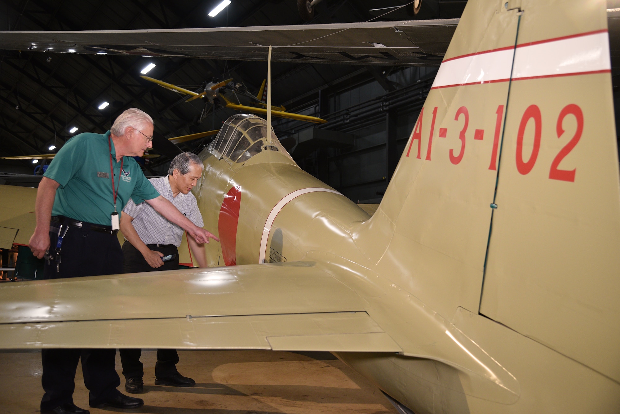 Photo of two people at Japanese Zero aircraft from World War II.