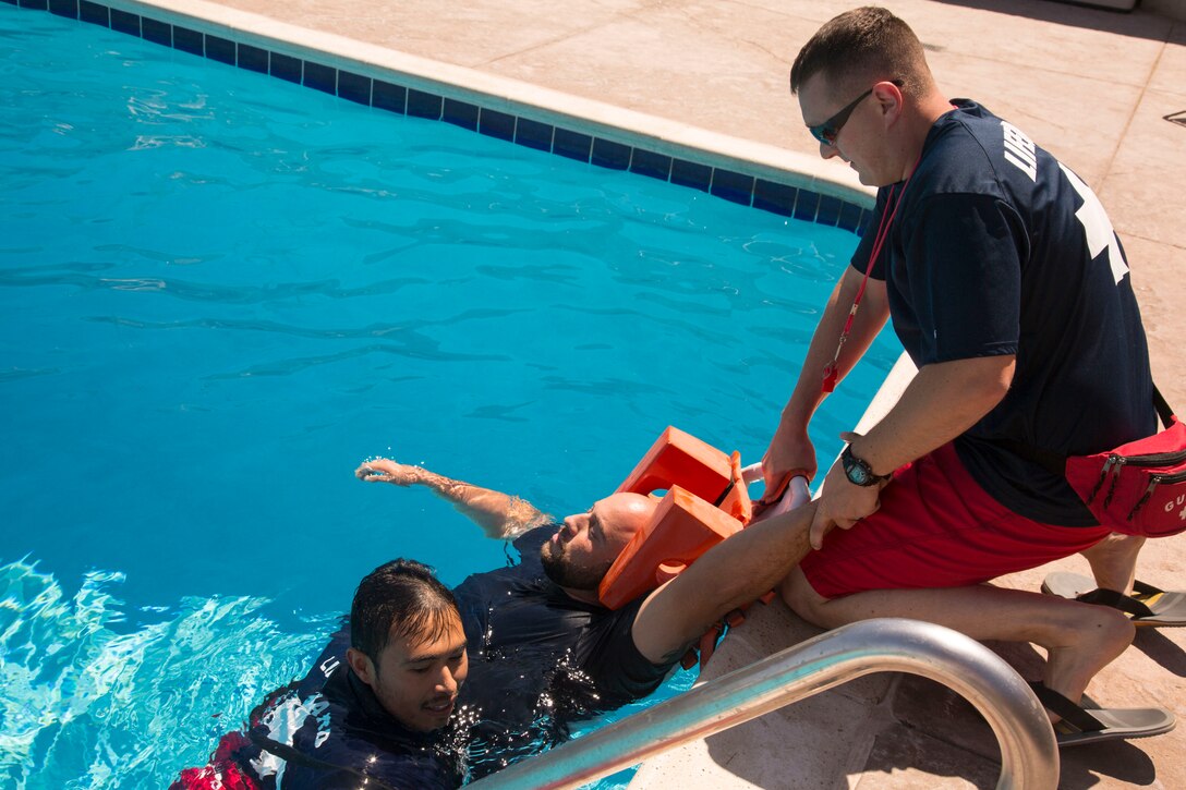 (Left) Primary lifeguard Francisco Cadillo ensures drowning “victim” Axel Rivera, lifeguard supervisor, is in place on the rescue backboard and one of Rivera’s arms is held firmly by Sgt. Maxim Krymov, volunteer Marine lifeguard, while Cadillo gets out of the pool to help Krymov pull the backboard up on to the pool deck. The Oasis Pool lifeguards and rescue elements of the Marine Corps Fire Department participated in the Emergency Action Plan training exercise August 27.