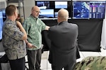 IMAGE: Glenn White (center), Office of Naval Research, discusses Mentor Station “real time” data analytics to John Fiore, Naval Surface Warfare Center Dahlgren Division technical director. The briefing occurred during an Advanced Navigation Team Shipboard Simulation Phase 1 system demonstration in the command’s Naval Simulation Center.