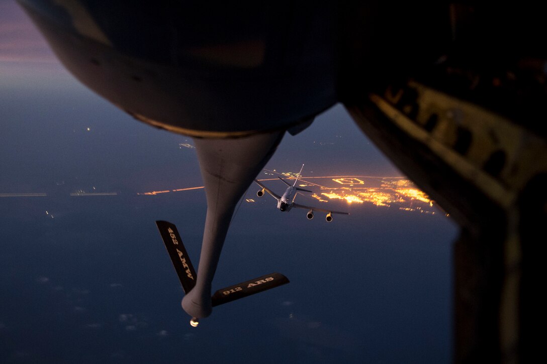A large military aircraft approaches the back of another aircraft at night.