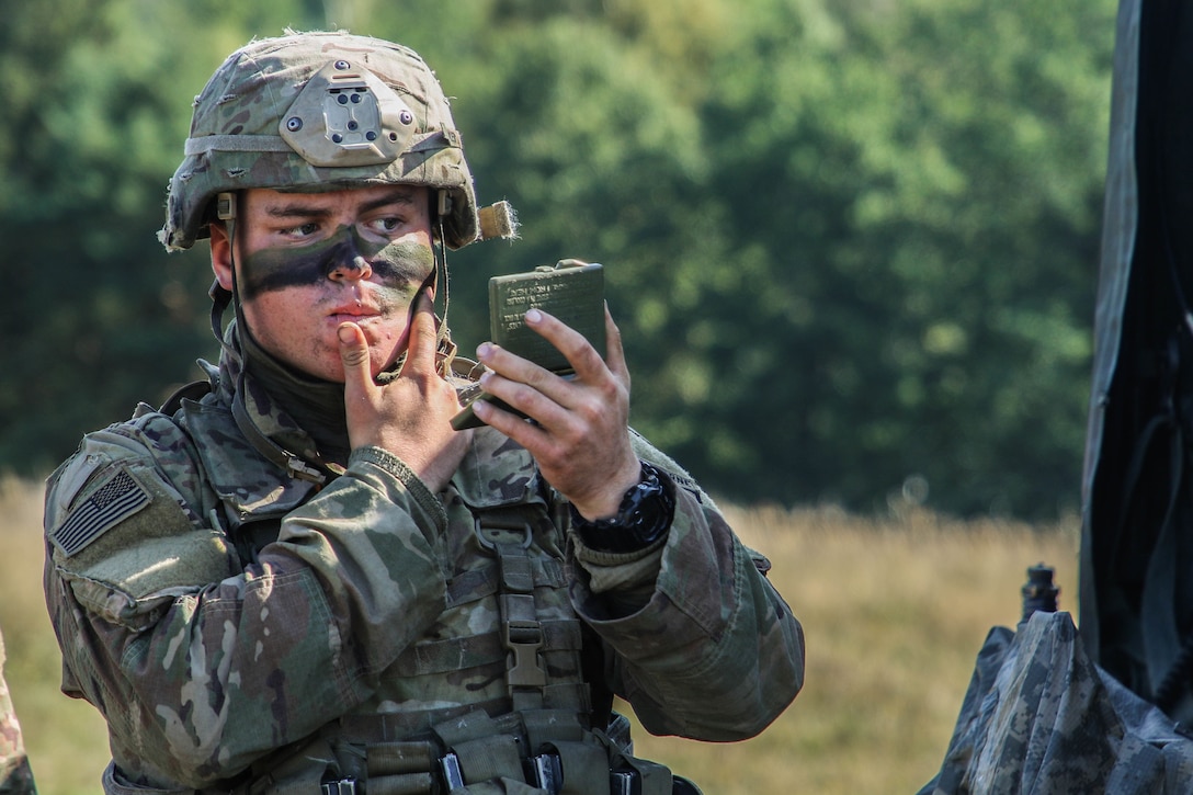 A soldier puts paint on his face while looking into a small mirror.