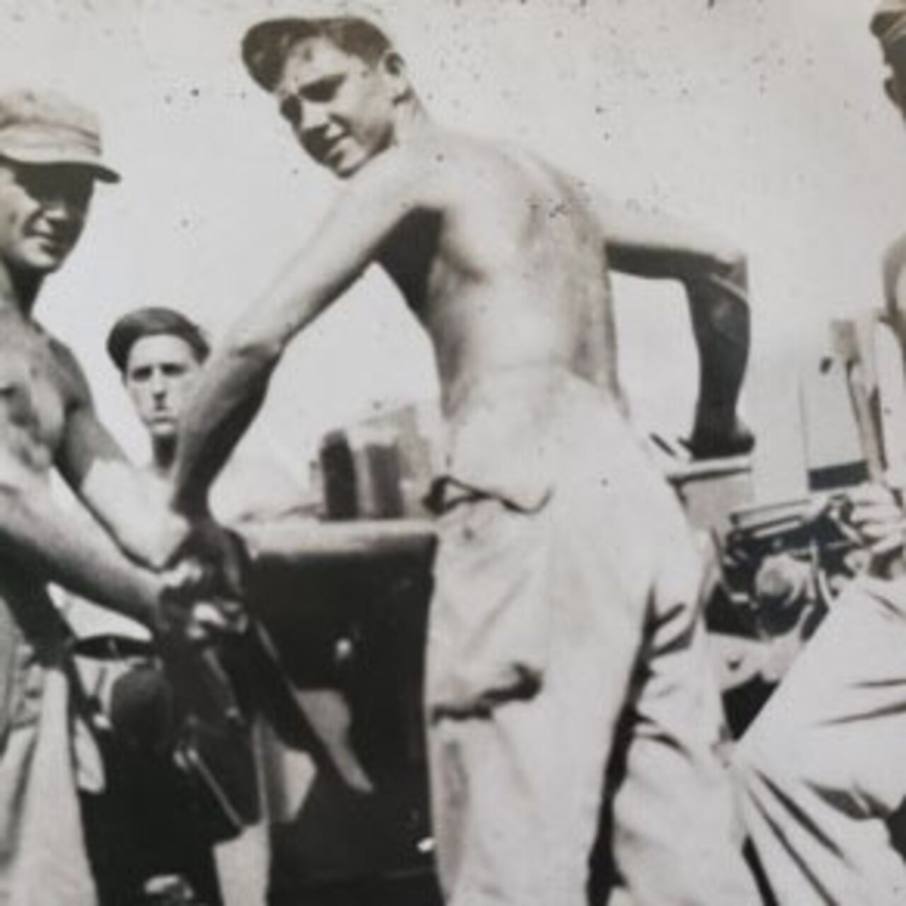 In a historic photo, a shirtless man poses for a photograph with a battery gun.