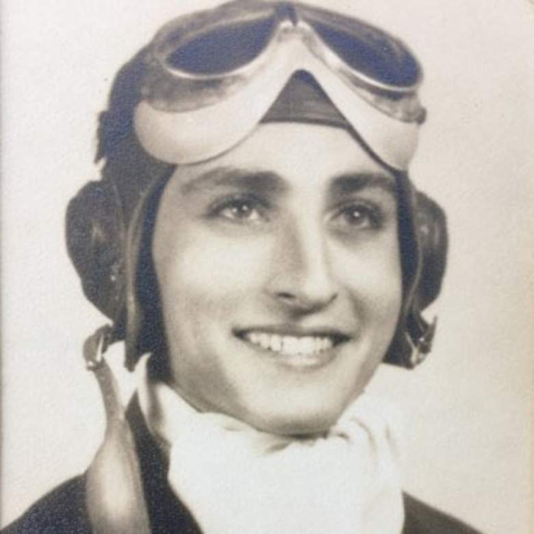 An old photo shows a young man with a broad smile dressed in an old-fashioned pilot’s uniform and goggles.
