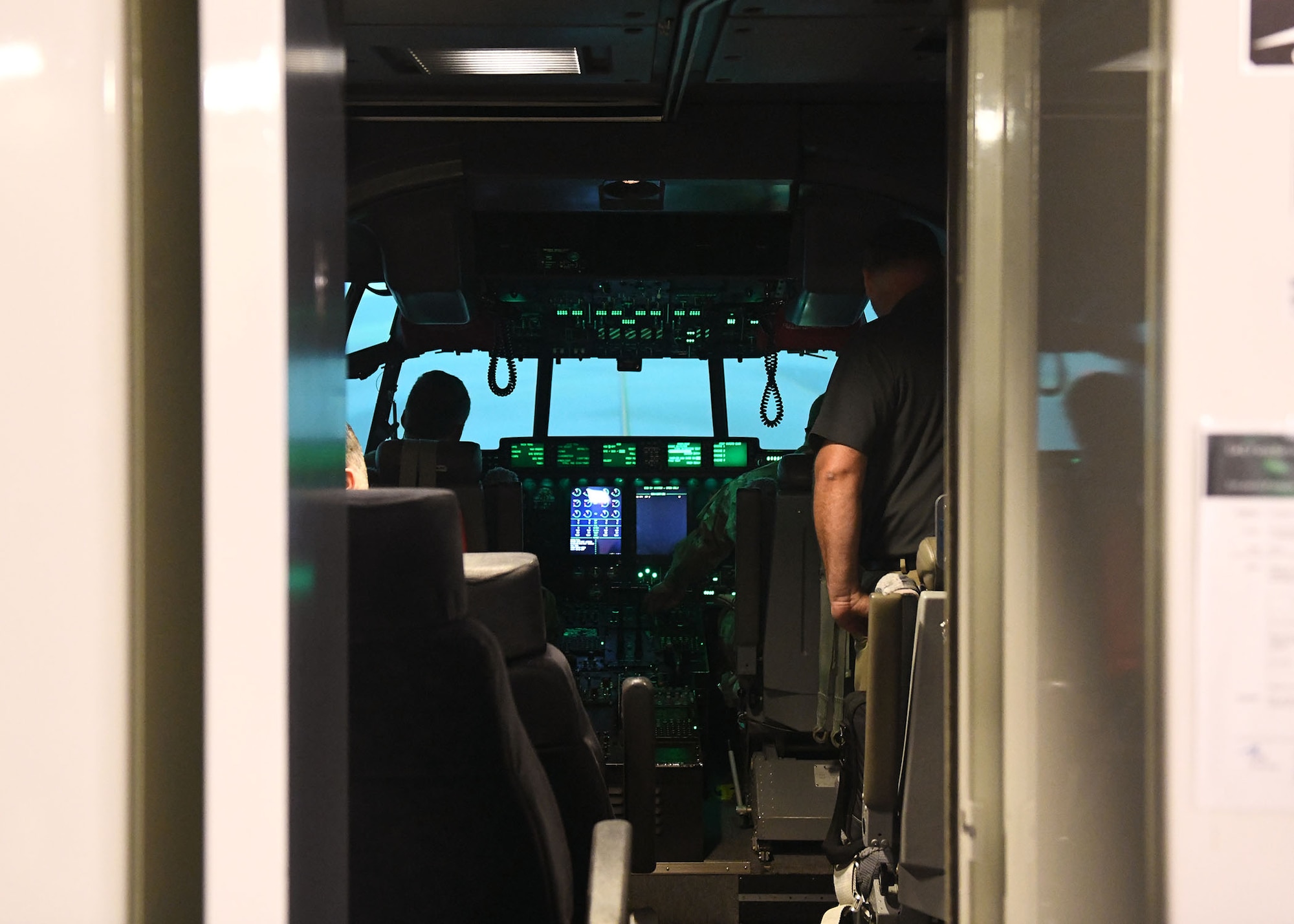Two men sit in front of the controls of a simulator that is made to look like the inside of a plane.