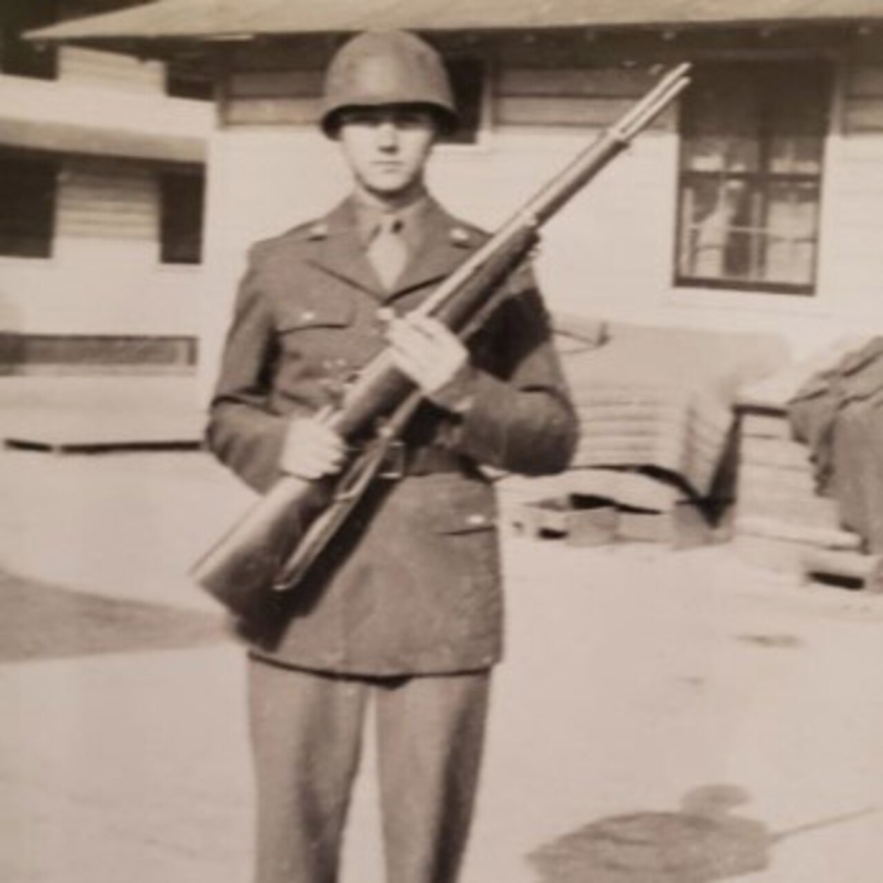 A young man dressed in an Army uniform poses hold up his rifle for a photo.