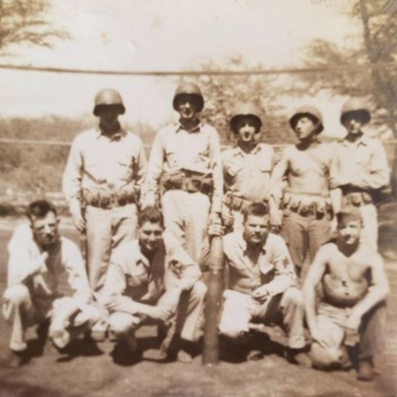 Nine men dressed in military uniforms pose for a photo.