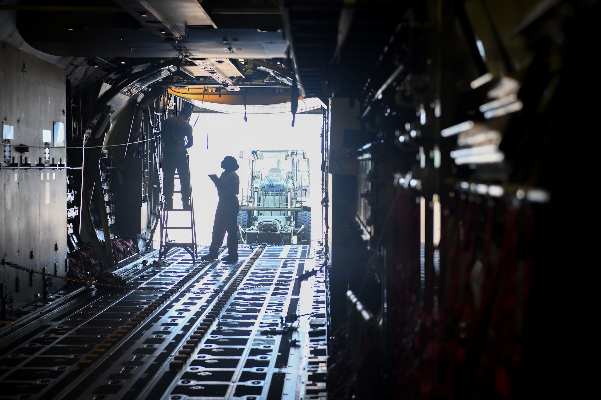 A woman looks up at a man on a ladder inside a plane simulator.