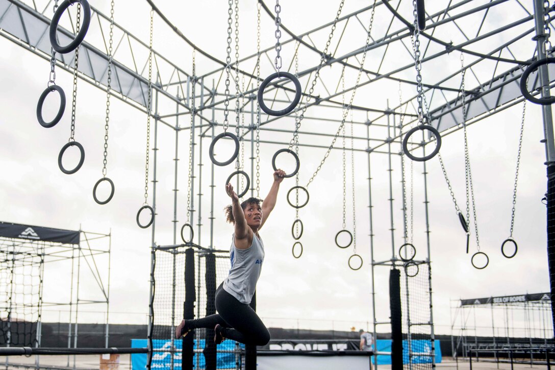 An airman swings on rings hanging from a metal structure.