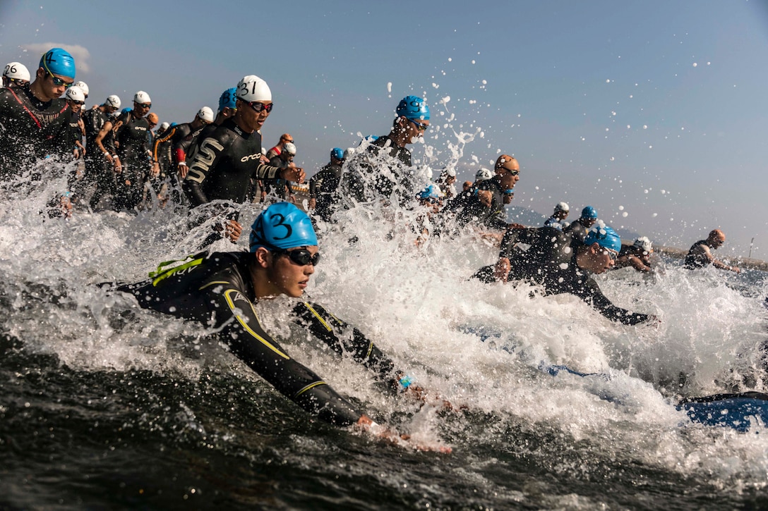 Swimmers in wetsuits splash in ocean waves.