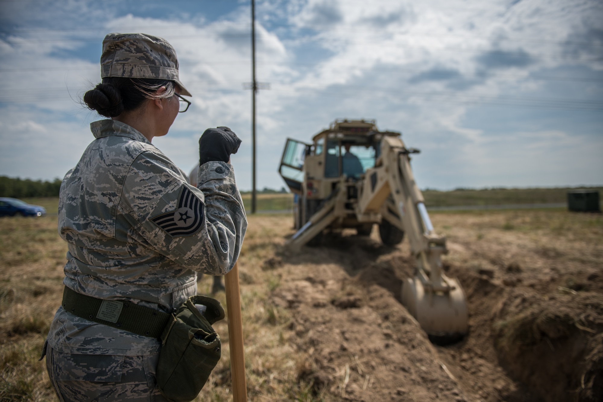 U.S. Air Force Reserve Citizen Airman Tech. Sgt. Tiana Corpuz looks on from a safe distance as Tech. Sgt. Casey Goodaker operates a backhoe to unearth a simulated water-main needing repairs during field training, Sept. 10, 2019 at the Sparta National Guard training area, Sparta, Illinois. The 932nd Civil Engineer Squadron spent two days at the training facility using the space for heavy equipment training, something they are not able to perform at Scott Air Force Base during unit training assemblies. (U.S. Air Force photo by Master Sgt. Christopher Parr)