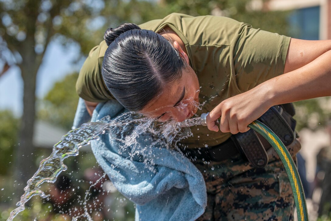 A Marine leans over and splashes her face with water from a hose she's holding outside.