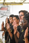 young men and women hold up their right hand to take an oath to enlist in the Army