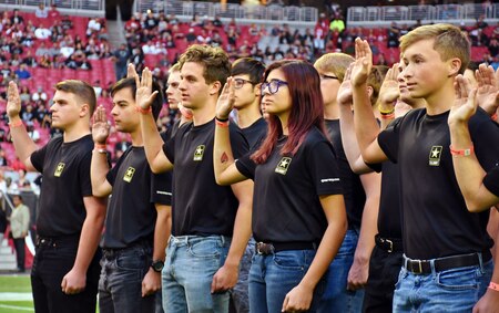 group of young men and women hold up their right hands as part of taking the oath of enlistment.