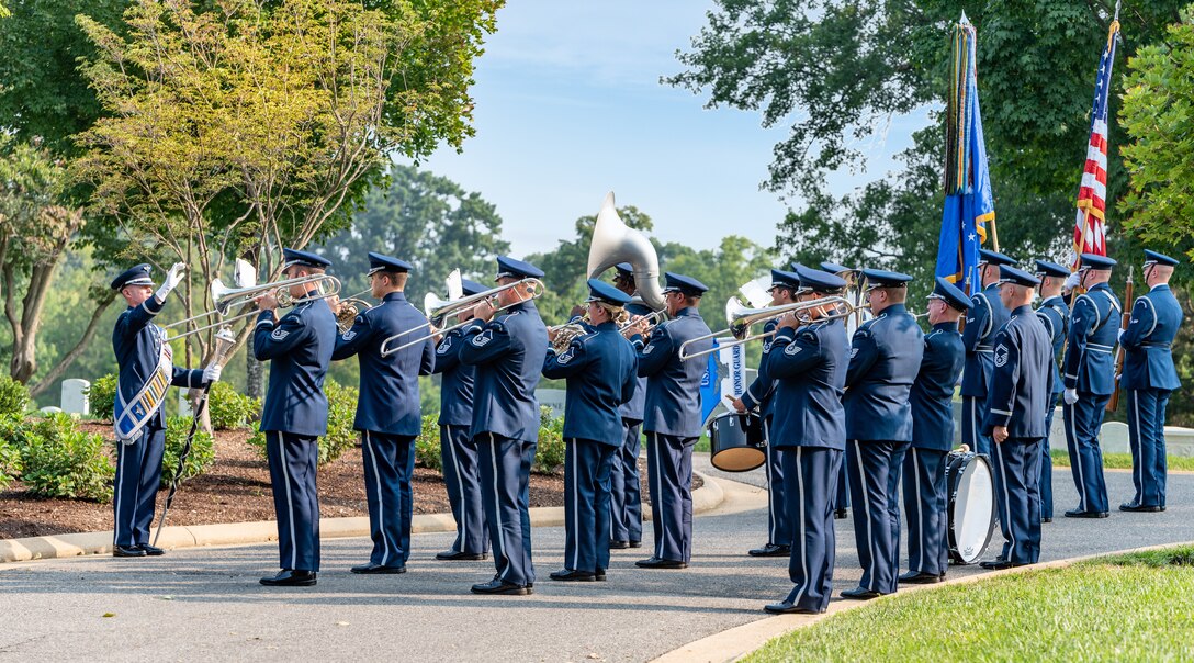 Several band members playing brass instruments face their drum major, who is conducting them with a mace in hand.