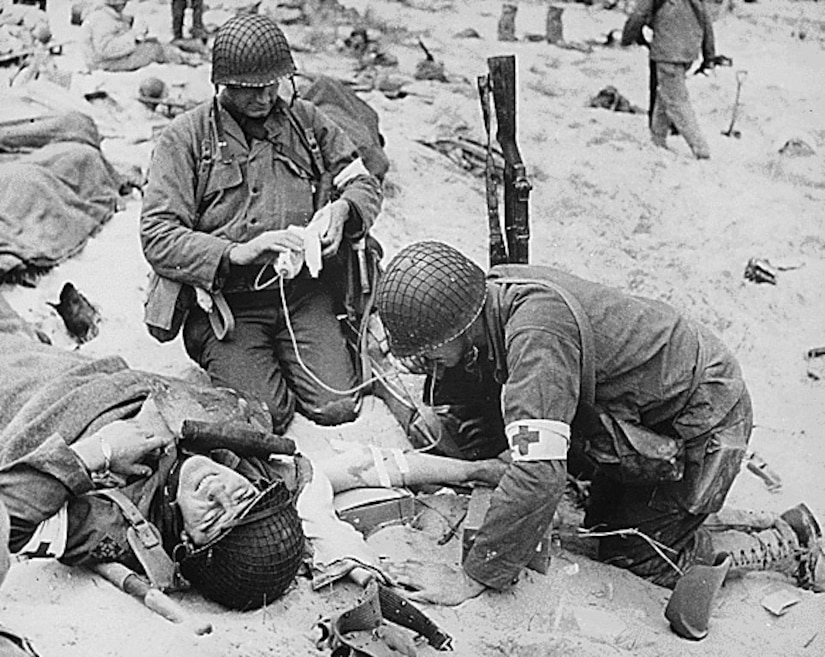 Combat medics wearing the Red Cross armbands put an IV into the arm of a soldier on the battlefield in France during World War II.