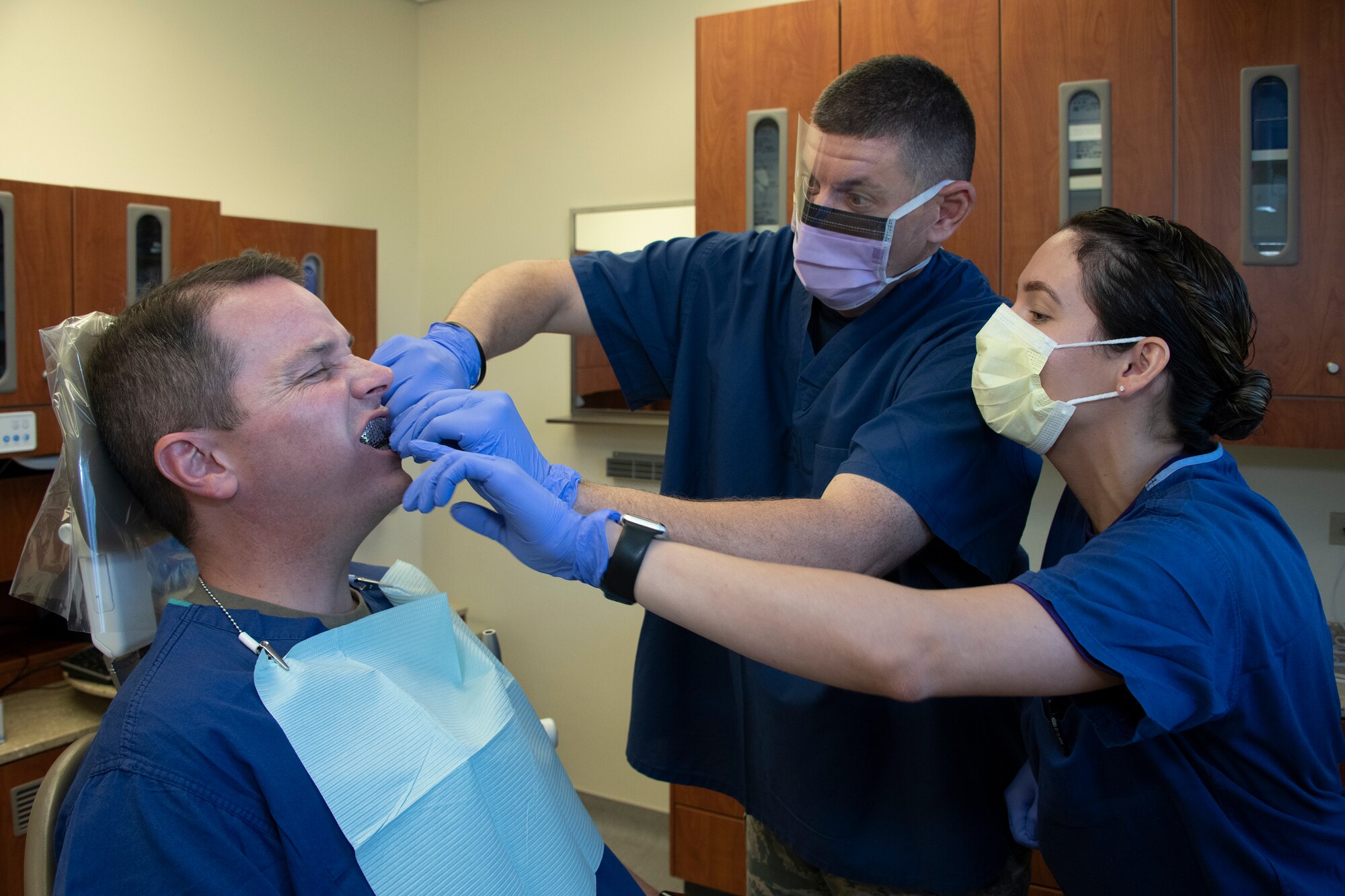 U.S. Air Force Col. Jeffrey Nelson, left, 60th Air Mobility Wing commander, undergoes a dental procedure done by Chief Master Sgt. Derek Crowder, 60th AMW command chief, and Senior Airman Rosemarie Rivera, 60th Dental Squadron dental assistant, as part of Leadership Rounds Sept. 13, 2019, at David Grant USAF Medical Center, Travis Air Force Base, California. The Leadership Rounds program involves wing leadership interacting with Airmen to get a detailed view of each mission performed at Travis AFB. (U.S. Air Force photo by Heide Couch)