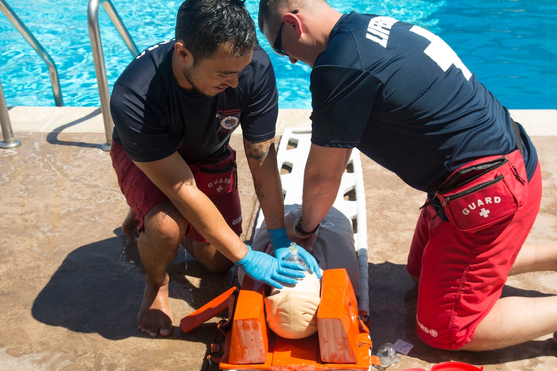 Francisco Cadillo, primary lifeguard, has delivered two breaths to a breath tube apparatus to the mouth of the drowning victim, in this case a resuscitation training manikin, as Sgt. Maxim Krymov, volunteer Marine lifeguard, delivers 30 chest compressions to the victim during an Emergency Action Plan training exercise in conjunction with rescue elements of the Marine Corps Fire Department. The two breaths and 30 - compression cycle continues until the victim is revived or fire department personnel arrive to take over the rescue effort.