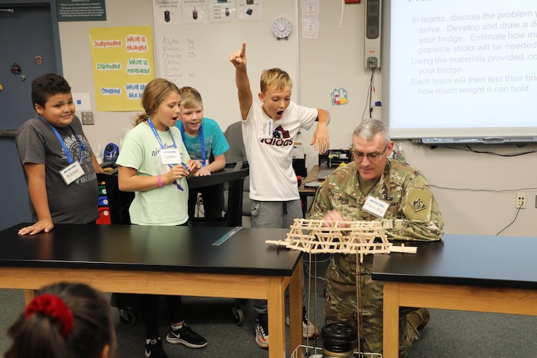 “Team Delta” students from Armel Elementary School in Frederick County, Virginia, react with surprise as their popsicle stick bridge sets a new loadbearing record for the Winchester, Virginia, STARBASE Program as Col. Stephen Bales, a civil engineer and Deputy Commander for the U.S. Army Corps of Engineers Transatlantic Division, loads on more weights. Bales gave an engineering presentation to the students and explained the use of triangles in design. The kids took his training to heart when building their bridge, which was able to support 62 pounds before it collapsed.