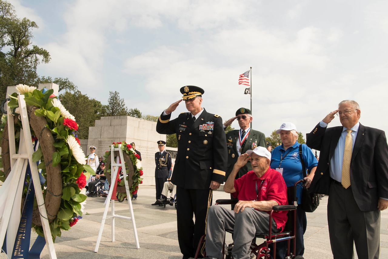 A veteran in a wheelchair and four other people salute a wreath.