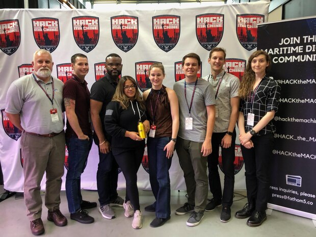 At the 2019 Hack the Machine event held in New York City, Sept. 6-8, members of the first place winning team, "Ahh Ship!" in the educational option of track one, "Hack the Ship," from left to right, Pete Frye, Eric Monette, Emmuel Delgado, Courtnee Mendes, Hanna Salian, Ian Wilson, Chris Draper, and Kiera Wells. The golden water bottle was used in lieu of a trophy.