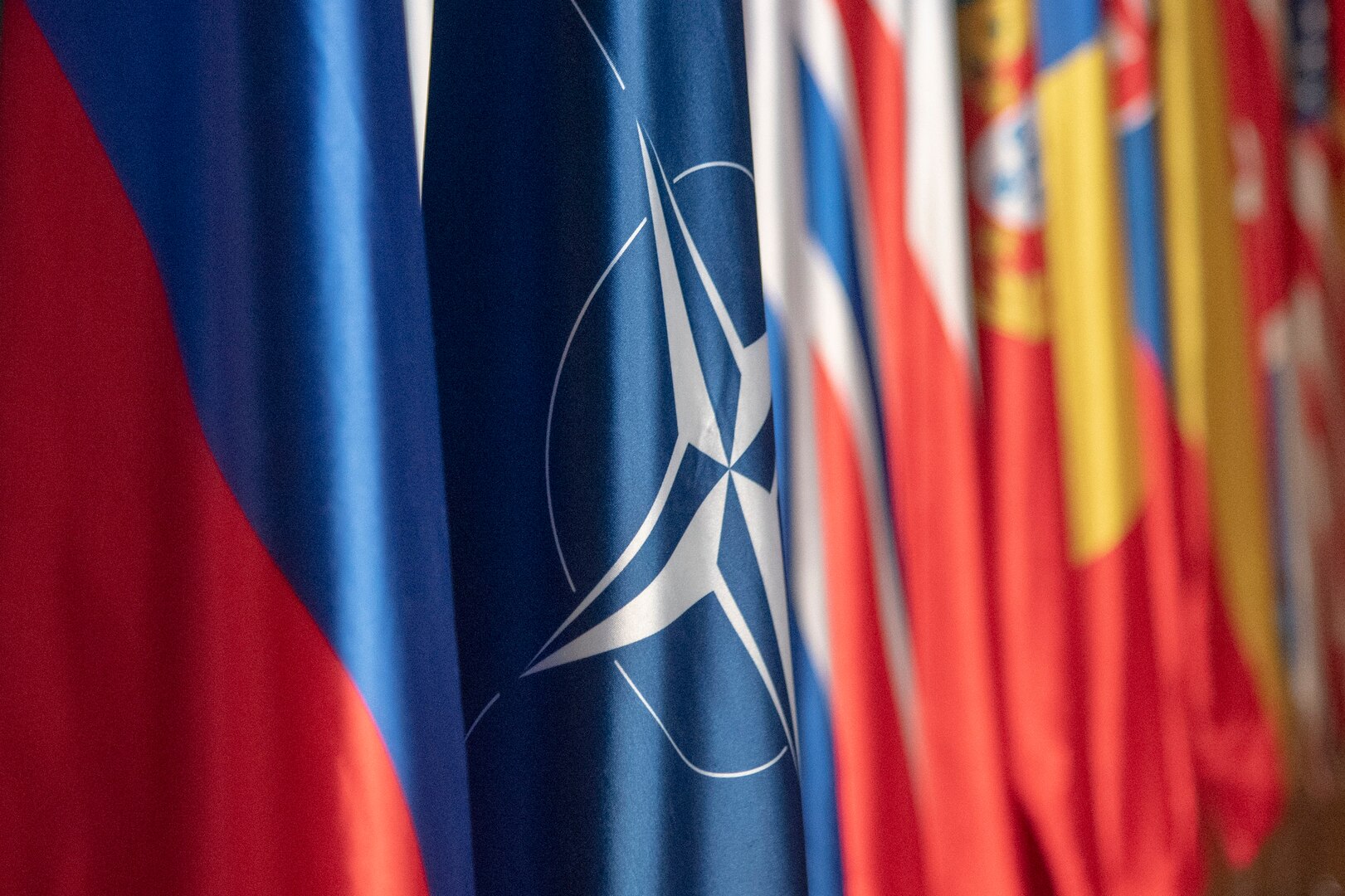 The NATO flag and others are displayed in a row in a room.