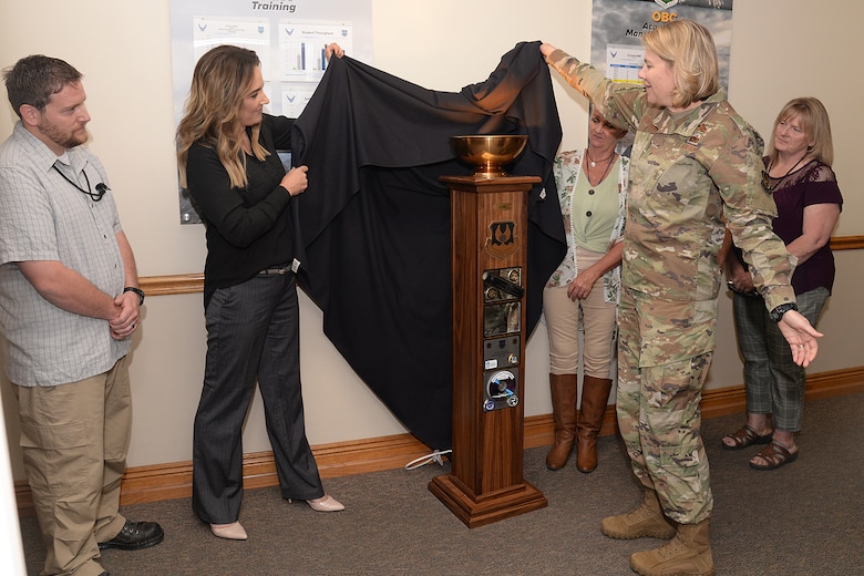 Brittney Starnes, OBWC chief (left), helps Brig. Gen. Cauley von Hoffman, Ogden Air Logistics Complex commander, unveil the L-A-M-P Award trophy Sept. 10, at Hill Air Force Base, Utah. The award is a traveling trophy which will is presented each month to the Complex’s most outstanding unit or team.