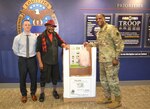 Army Brig. Gen. Gavin Lawrence, DLA Troop Support commander, right, Leonard Shannon, DLA Troop Support material handler, center, and Shaun Eagan, DLA Troop Support public affairs specialist, pose in front of a Feds Feed Families donation box Sept. 3, 2019 at DLA Troop Support in Philadelphia.