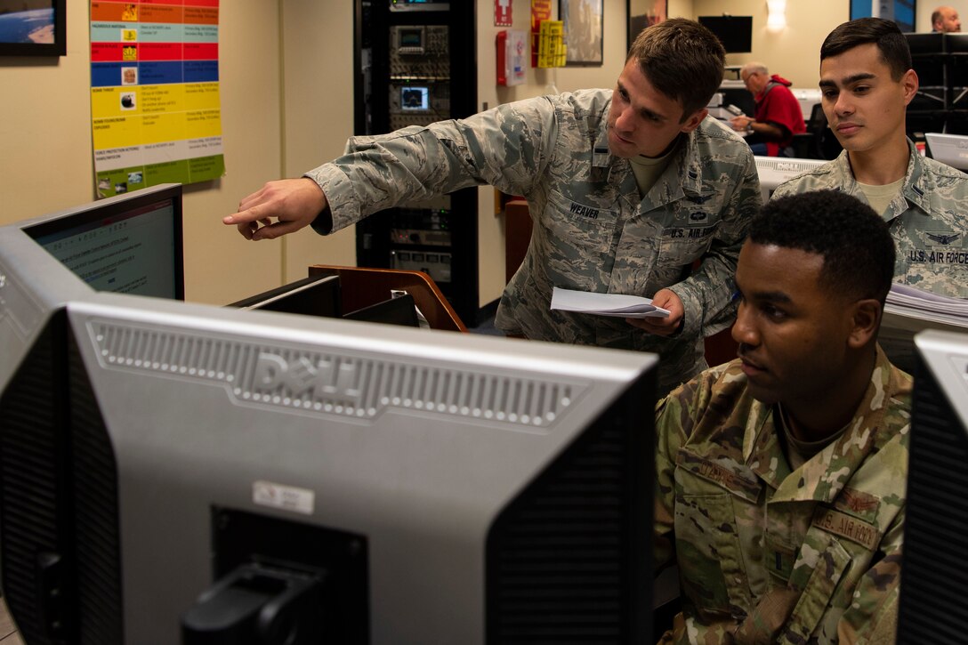 Three airmen look at monitors.