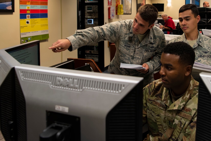 Three airmen look at monitors.