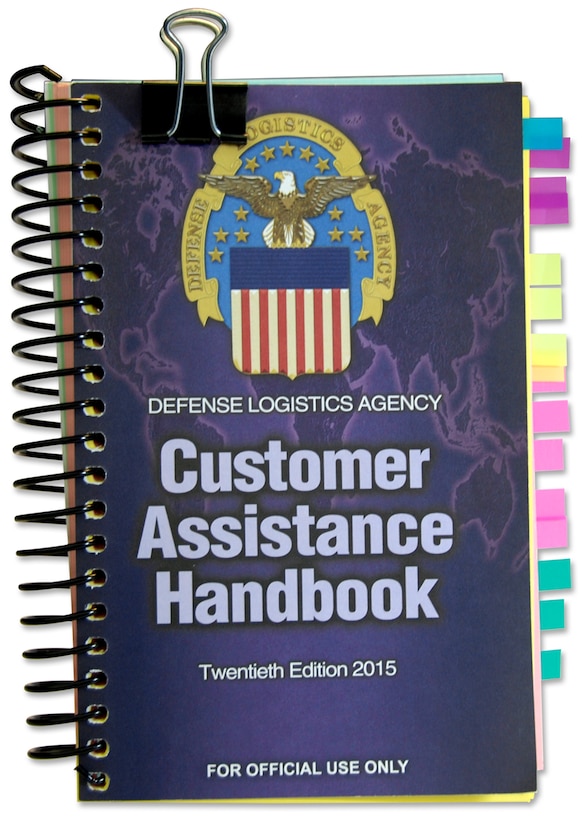 Isolated image of DLA Customer Assistance Handbook with large metal clip on top and multicolored tabs on the side.