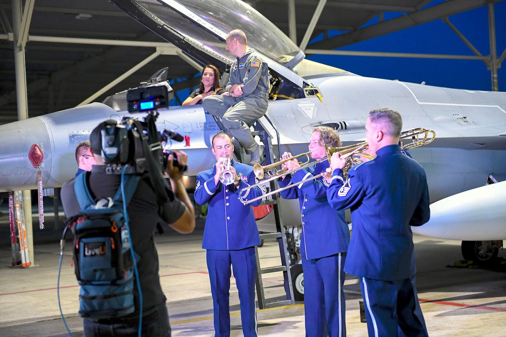 Members from United States Air Force Band of the West play in front of an F-16 Fighting Falcon, an aircraft assigned to the 149th Fighter Wing, while local weather reporter Jeannette Calle and 502nd Operations Support Squadron commander, Lt. Col. Benjamin Mather, talk in the background before the live broadcast at Joint Base San Antonio-Lackland Sept 18. Local weather reporters decided to conduct a live weather broadcast at the JBSA-Kelly Field Annex in honor of the Air Force’s 72nd birthday.