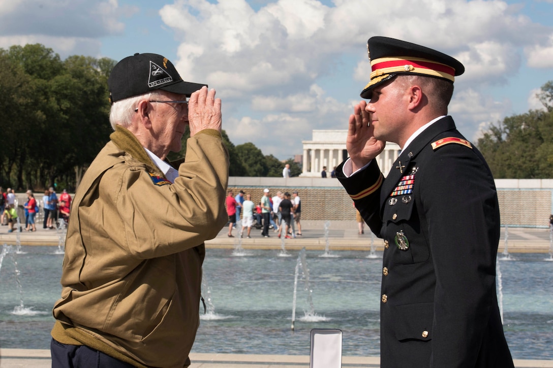 A soldier and a veteran salute each other.