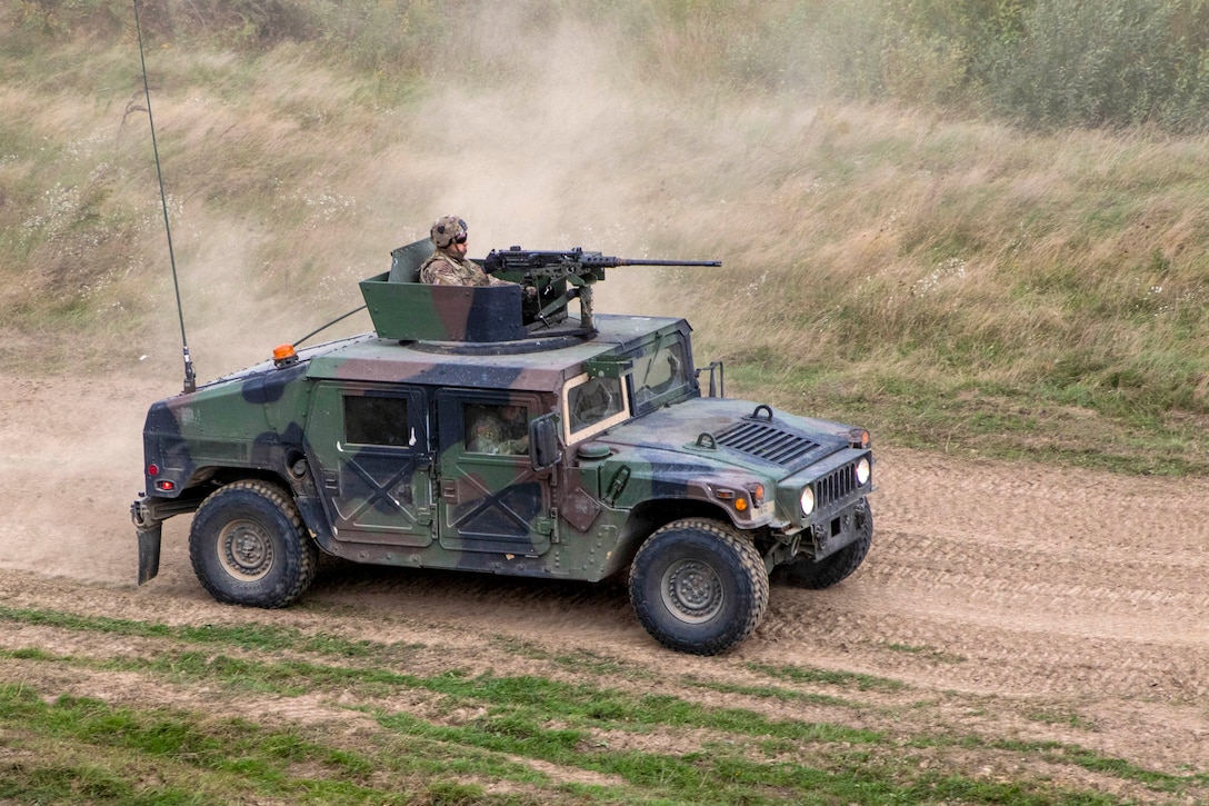 Soldiers drive in a Humvee on a dusty dirt road.