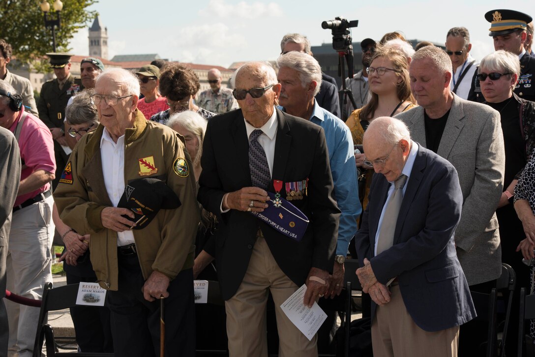 Three veterans stand together at an outdoor ceremony.