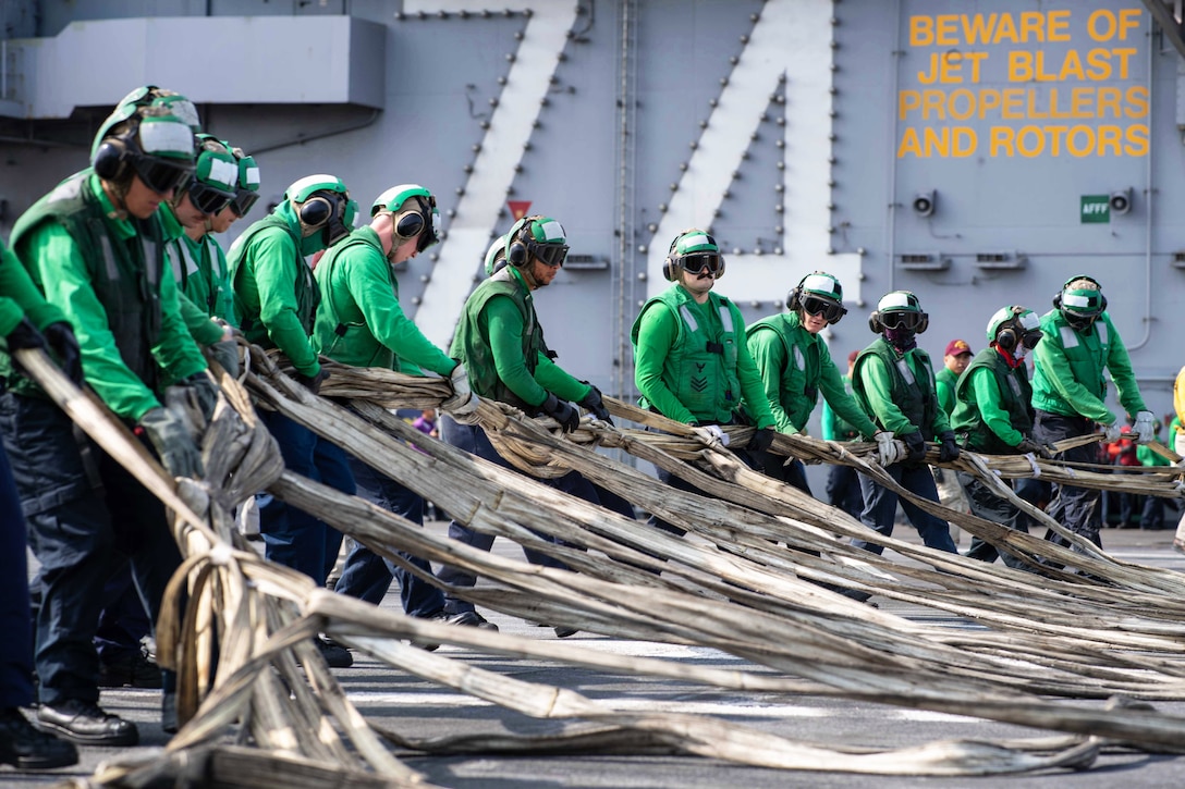 Sailors in green uniforms standing in a line handle material for a barricade.