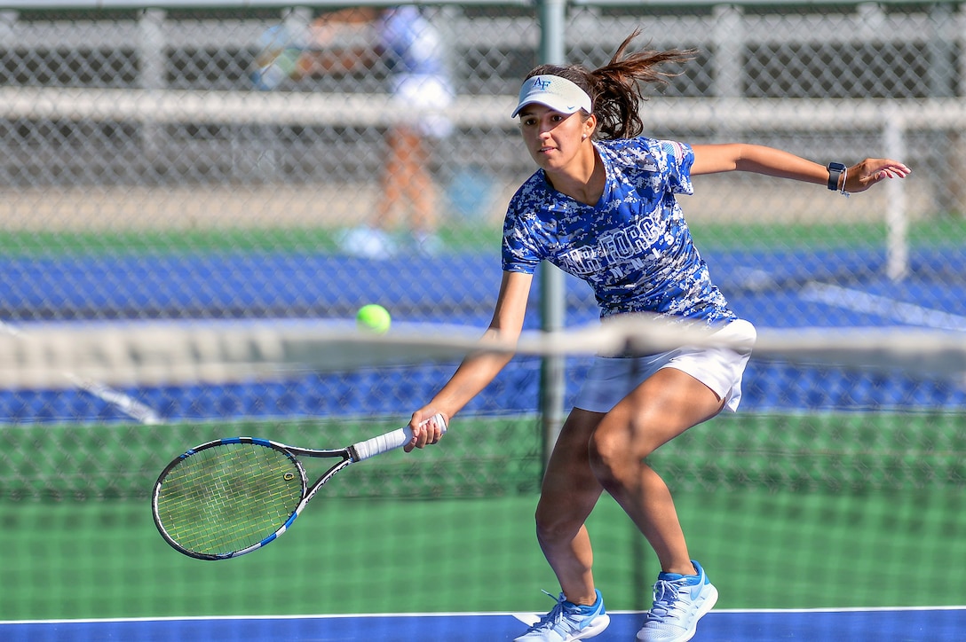 An Air Force cadet hits a tennis ball on a court.