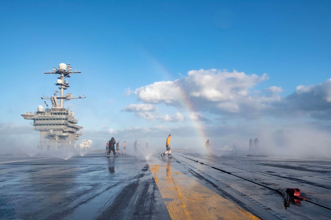 A rainbow is seen through mist as people patrol the deck of a ship.